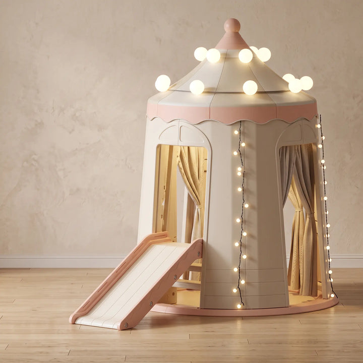 Creamy beige and pastel pink castle playhouse with an integrated white slide, decorative string lights, and fabric curtains, showing overall dimensions.