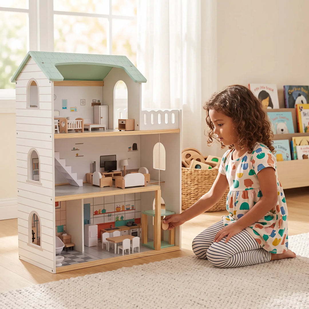 A young girl plays with a three-story wooden dollhouse featuring a mint green roof and white exterior siding, showcasing detailed interior rooms and miniature furniture.