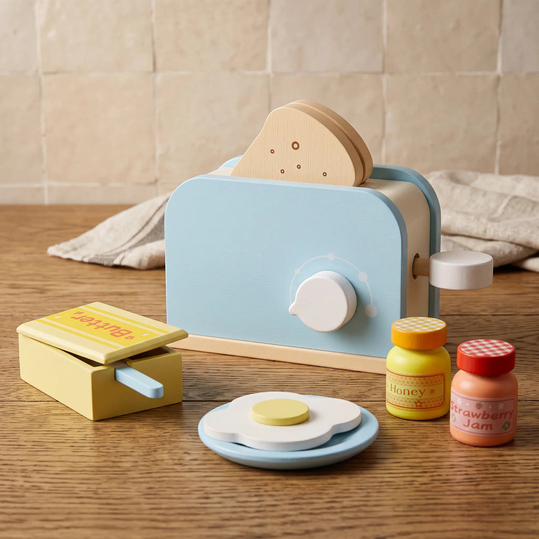 ToyHare wooden kitchen playset accessories including a blue and white toaster with toast, butter box, fried egg, honey, and strawberry jam jars, arranged on a wooden table.