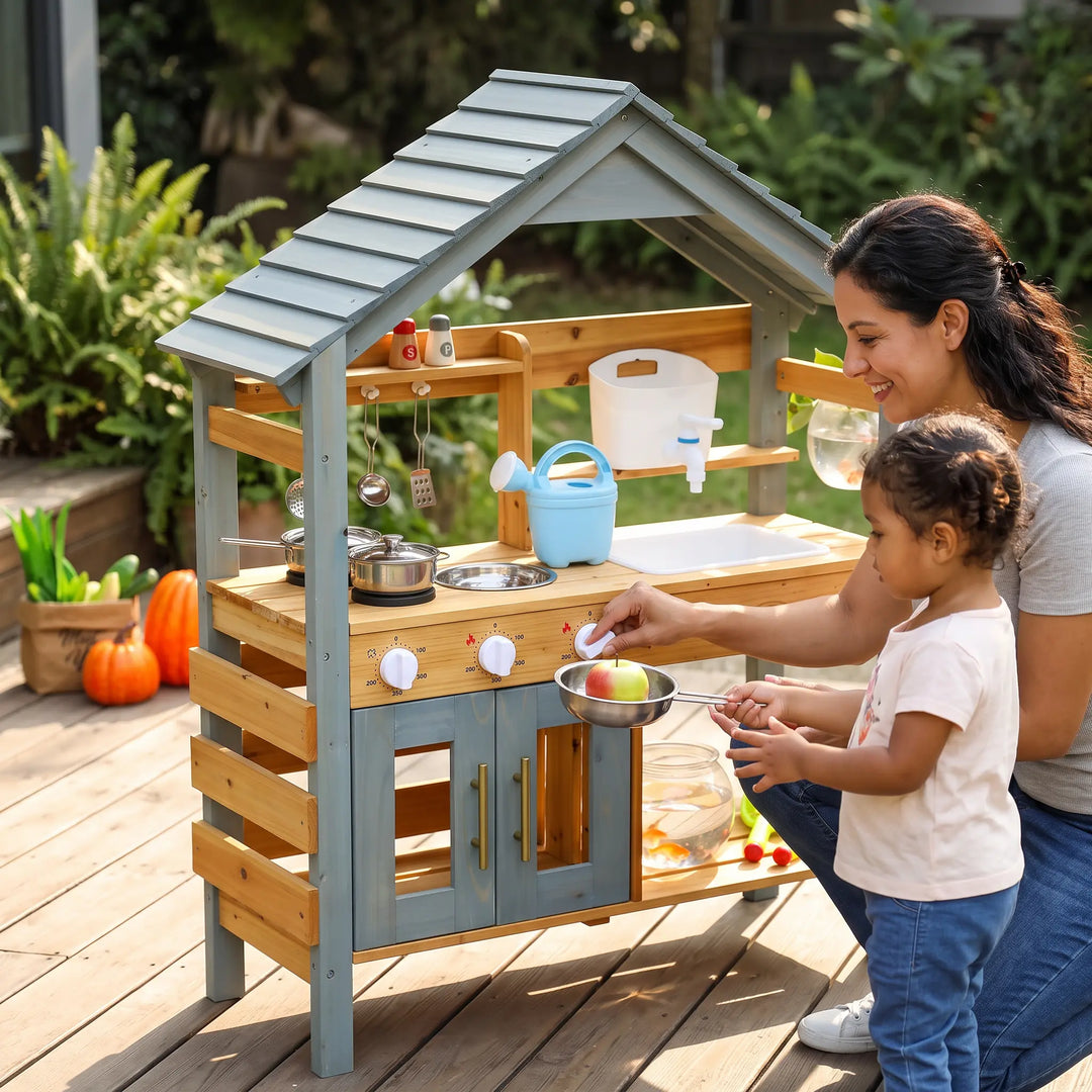 Mother and child playing together with a ToyHare wooden outdoor kitchen playset on a wooden deck, featuring a light blue roof, natural wood finish, and included accessories.