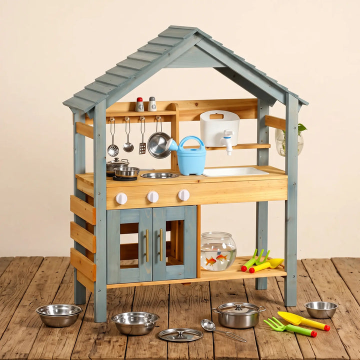 ToyHare wooden outdoor play kitchen with a slatted light blue roof, natural wood structure, and blue cabinet doors. Features include a white sink, faucet, burner knobs, and hanging utensils, with play accessories and a fishbowl on the side.