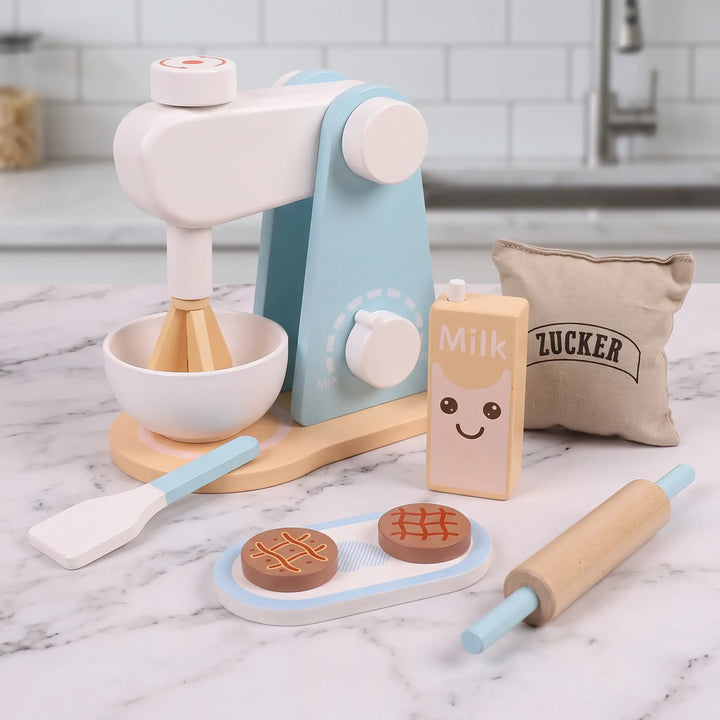 Wooden kitchen playset mixer with bowl and whisk, alongside play food, rolling pin, spatula, and milk carton on a wooden surface.