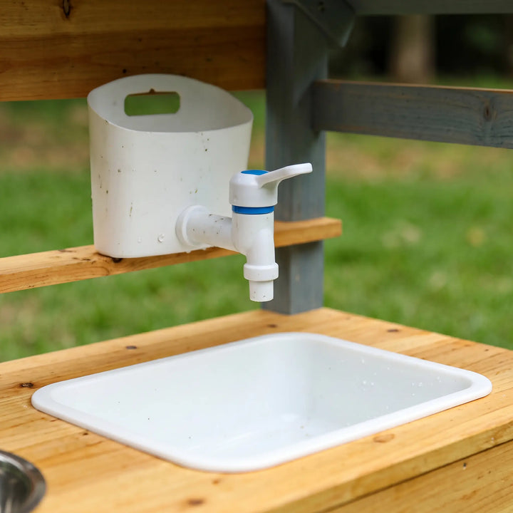 Close-up of a functional white faucet with blue accents and a white sink basin on a wooden shelf of an outdoor play kitchen.
